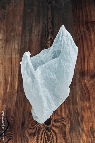 White empty plastic bag floating over wooden background. Collecting plastic waste to recycling. Concept of plastic pollution and too many plastic waste. Copy space at the top. Environmental issue