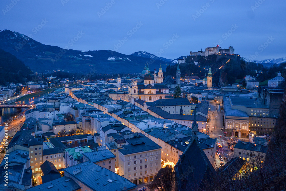 Salzburg evening cityscape with main Cathedral, Kollegienkirche and illuminated streets of old town on background of mountains in clouds