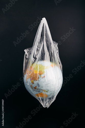 Globe in a plastic bag. Earth contaminated by plastic waste. Concept of plastic pollution and plastic waste. Globe over black background. Copy space for text