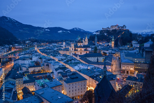 Salzburg evening cityscape with main Cathedral  Kollegienkirche and illuminated streets of old town on background of mountains in clouds
