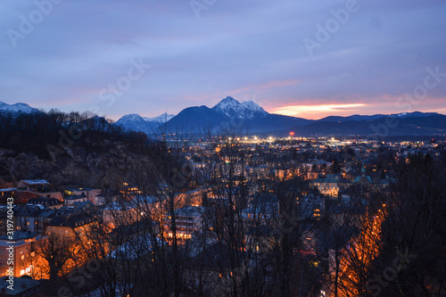 Salzburg evening cityscape with main Cathedral, Kollegienkirche and illuminated streets of old town on background of mountains in clouds