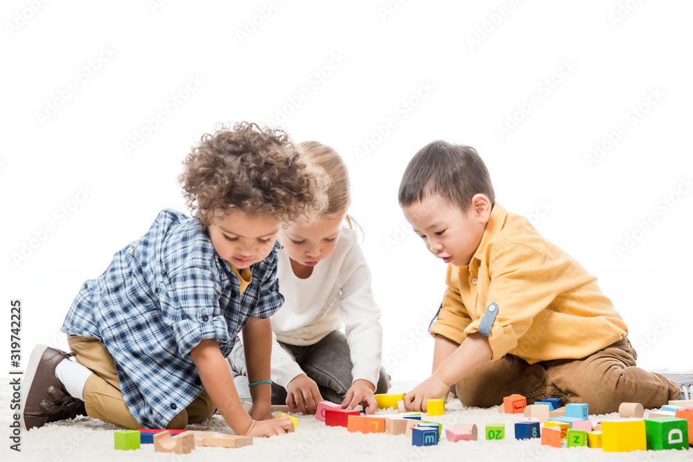 multiethnic children playing with wooden blocks on carpet, isolated on white multiethnic children playing with wooden blocks on carpet, isolated on white