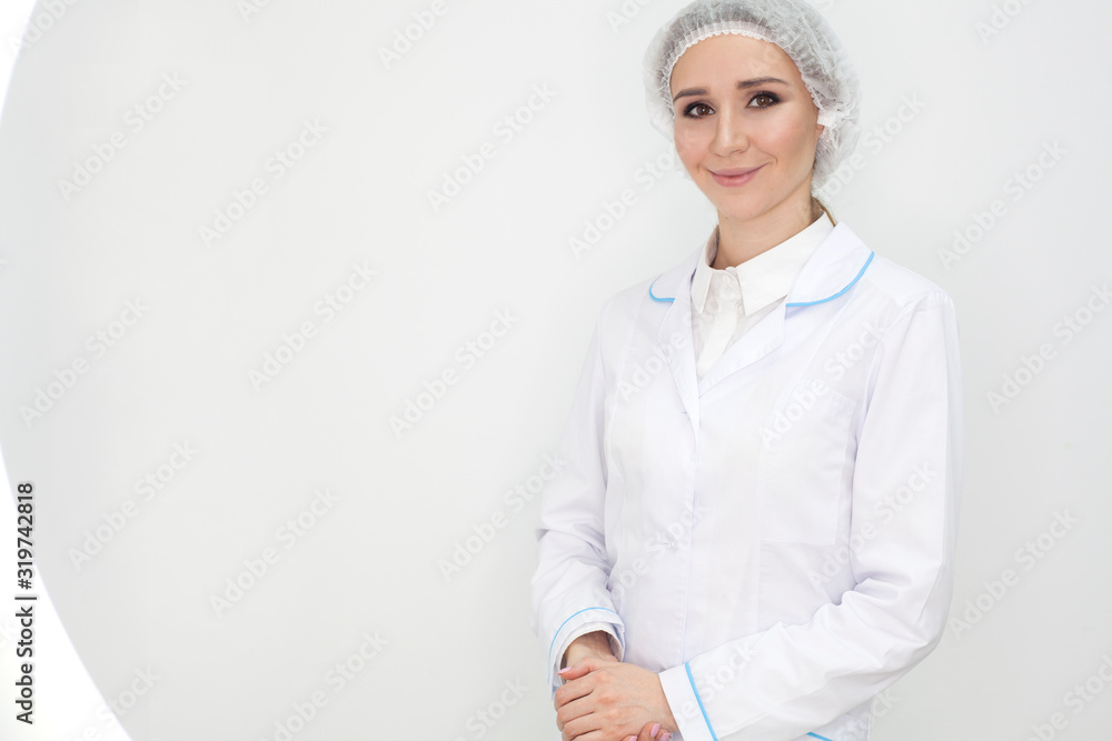 The doctor in a coat is isolated on a white background, the girl in a white coat smiles and looks into the frame, with copy space. Clinic advertising concept. The doctor in a coat is isolated on a white background, the girl in a white coat smiles and looks into the frame, with copy space. Clinic advertising concept.
