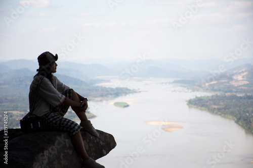 Asian thai woman travel visit and posing sitting on ridge stone of cliffs at Wat Pha Tak Suea temple with view of landscape of Nongkhai city and loas and Mekong river in Nong Khai, Thailand