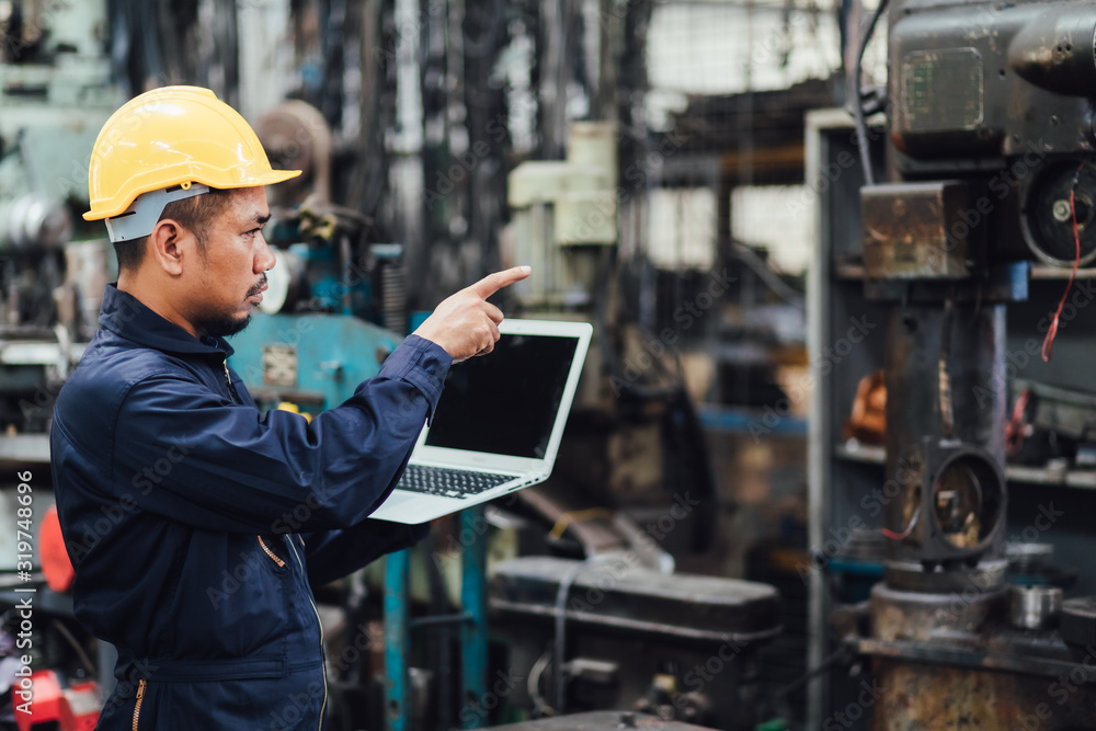Asian Chief Engineer in the Hard Hat and working on computer laptop about mechanical piece At old Factory Equipment. Asian Chief Engineer in the Hard Hat and working on computer laptop about mechanical piece At old Factory Equipment.
