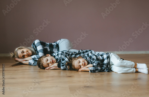 Obraz na płótnie Top view of mother and her two kids in identical clothes lying on floor with closed eyes. w salonie