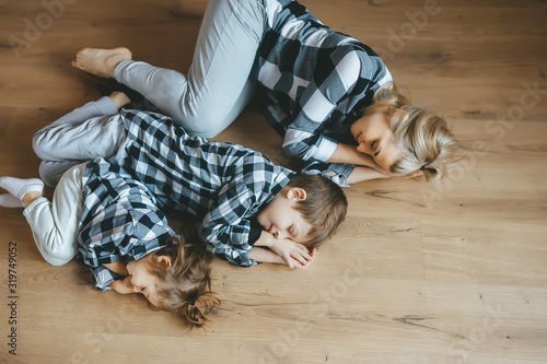 Obraz na płótnie Top view of mother and her two kids in identical clothes lying on floor with closed eyes. Top view w salonie