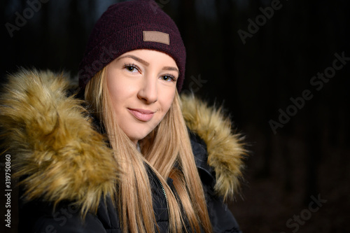 Young beautiful girl with blond hair. Portrait of an attractive girl with blond hair on dark blurred background. She smiles in the picture.