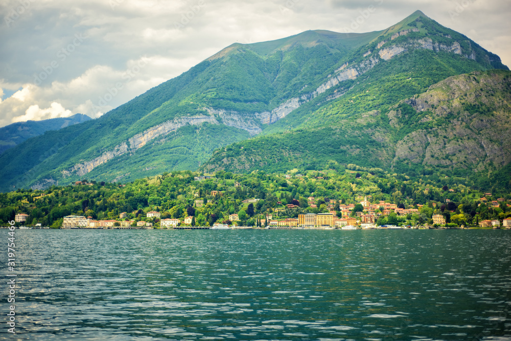 Amazing view of Como Lake, panorama of lake with small town and Alps mountains on background in cloudy day. Vacation on Como, Lombardy, Italy. Popular tourist destination. Italian city.