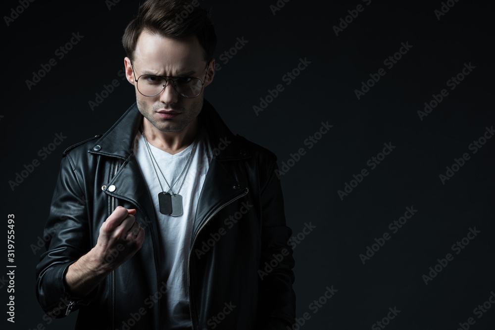 angry stylish brutal man in biker jacket showing fist isolated on black