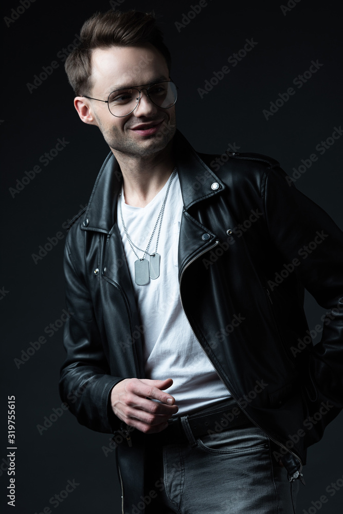 smiling stylish brutal man in biker jacket pointing with finger aside isolated on black smiling stylish brutal man in biker jacket pointing with finger aside isolated on black