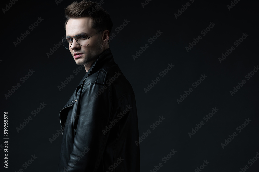 side view of stylish brutal man in biker jacket looking at camera isolated on black side view of stylish brutal man in biker jacket looking at camera isolated on black