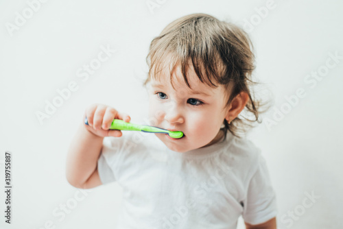 Little girl brushes her teeth with a toothbrush on a light background