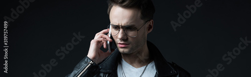 tense stylish man talking on smartphone isolated on black, panoramic shot