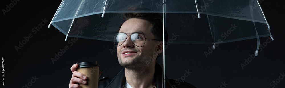 Obraz premium smiling stylish brutal man in biker jacket with umbrella and coffee to go isolated on black, panoramic shot