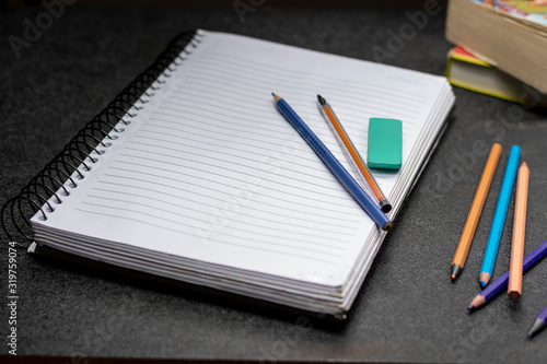 caderno com lápis caneta e borracha de apagar sobre uma superfície preta com alguns livro ao fundo   photo