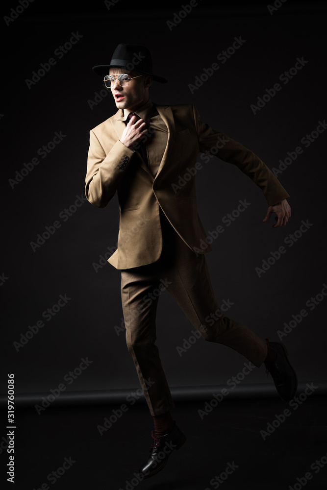 elegant man in beige suit, hat and eyeglasses running on black elegant man in beige suit, hat and eyeglasses running on black