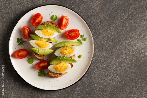 Avocado, egg on toast, tomatoes on plate. Top view on a dark background.
