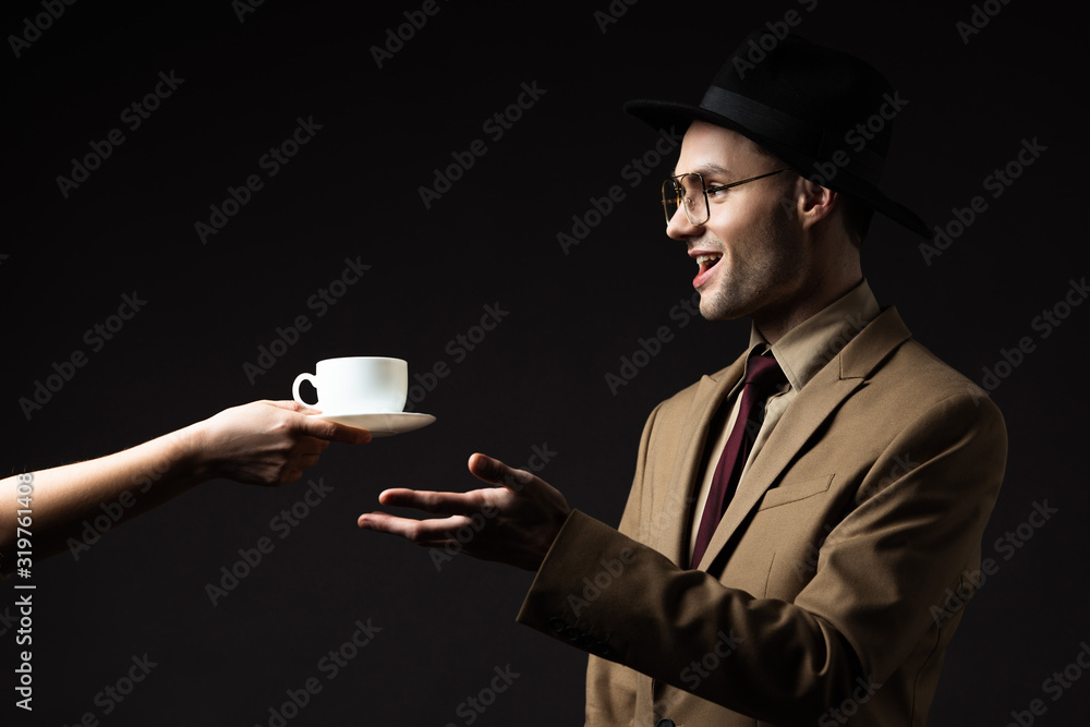 smiling elegant man in beige suit, hat and eyeglasses taking coffee from waiter isolated on black smiling elegant man in beige suit, hat and eyeglasses taking coffee from waiter isolated on black