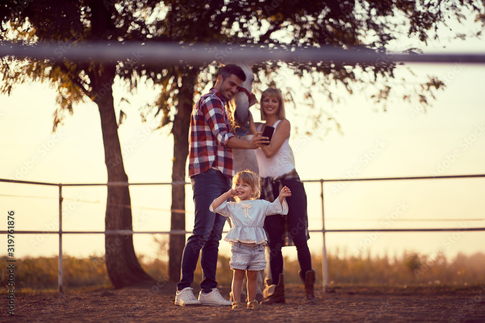 Fototapeta premium Parents with their daughter on a horse ranch . Family on countryside, sunset golden hour. Freedom nature concept.