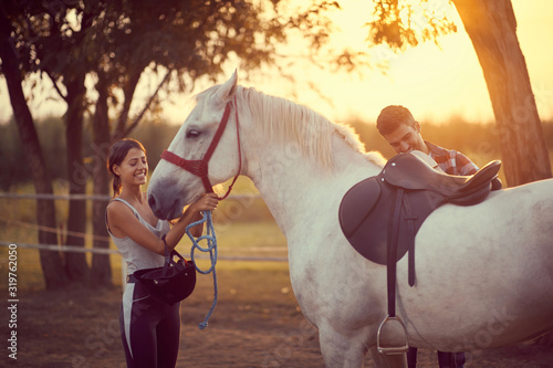 Man putting a saddle on a horse. Training on countryside, sunset golden hour. Freedom nature concept.