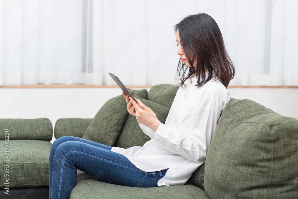 Obraz premium リビングでタブレットを操作する女性