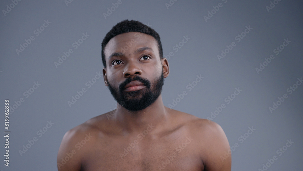 Fototapeta premium Portrait of topless sexy african american man using a virtual screen swiping pages in air. Young black guy with beard and fit body isolated on grey background.