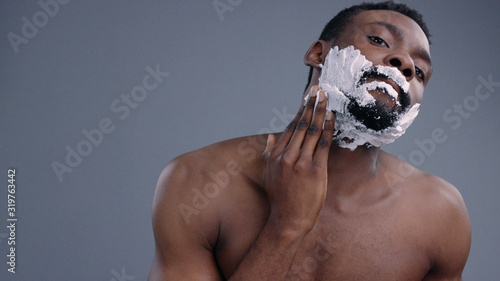 Billede på lærred Close-up of handsome young afro-american shirtless man shaving and applying cream on his face