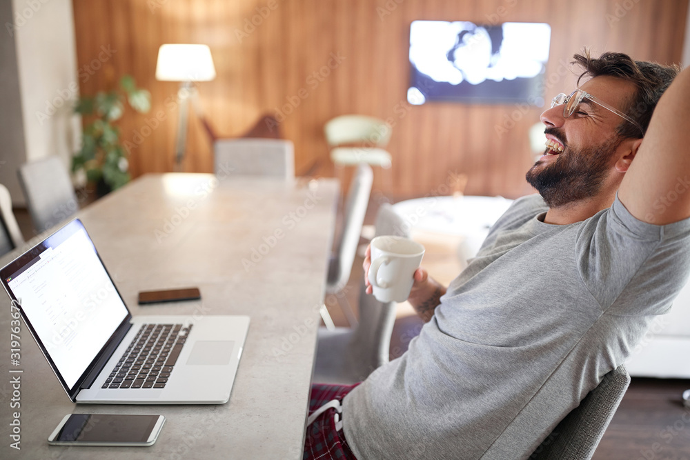Smiling man drink morning cup of coffee while working on laptop. Smiling man drink morning cup of coffee while working on laptop.