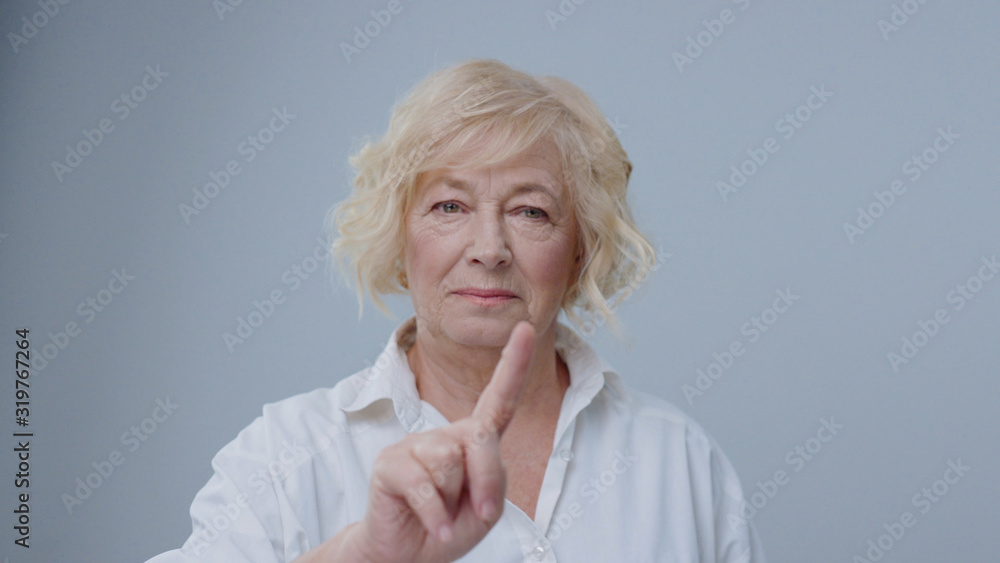 Cheerful blonde old woman using a virtual technology screen in air pointing with fingers and smiling of joy on light background. Cheerful blonde old woman using a virtual technology screen in air pointing with fingers and smiling of joy on light background.