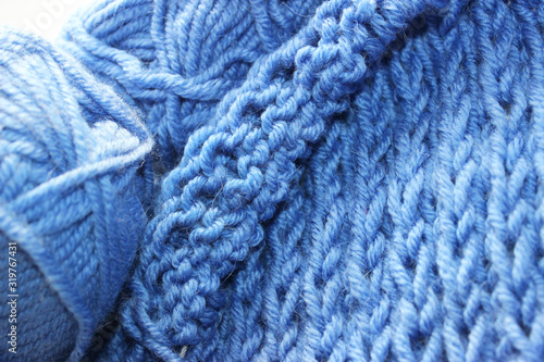 A piece of blue knitting with balls of yarn and knitting needles. Knitted woolen yarn fabric. Knitting project in progress concept. 