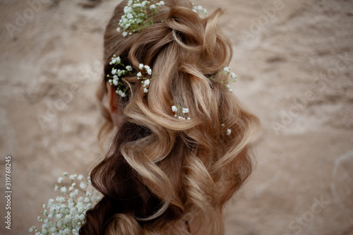 Blond woman with beautiful log hair on nude shoukders. The hairstyle of bride qith flowers , back view of salon hair do against wall. Care and beauty of hair