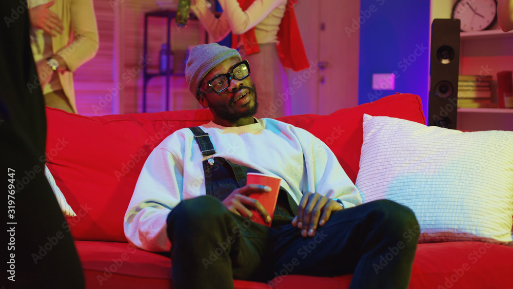 Obraz premium Handsome black guy relaxing on couch in cozy apartment drinking alcohol and celebrating great club party together at home.