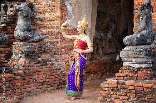 Portrait of an Asian Women in Thai Traditional dancer Clothes are Standing Against Ancient buddha statue. Ayuttaya Historical Park, Thailand Asia.