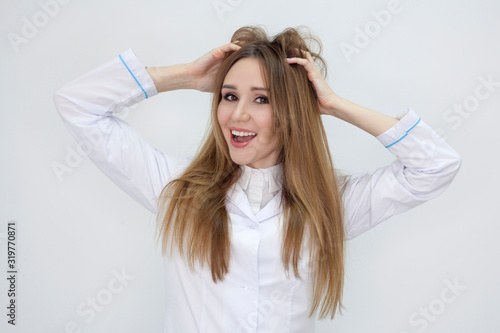 A girl in a medical uniform is happy, with wide eyes and a smile, holding her head in her hands, lifting her hair on her head. Concept of cosmetic services for hair or scalp and advertising of clinic.