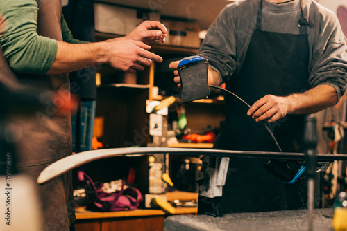 cropped view of worker giving wax iron to colleague in repair shop