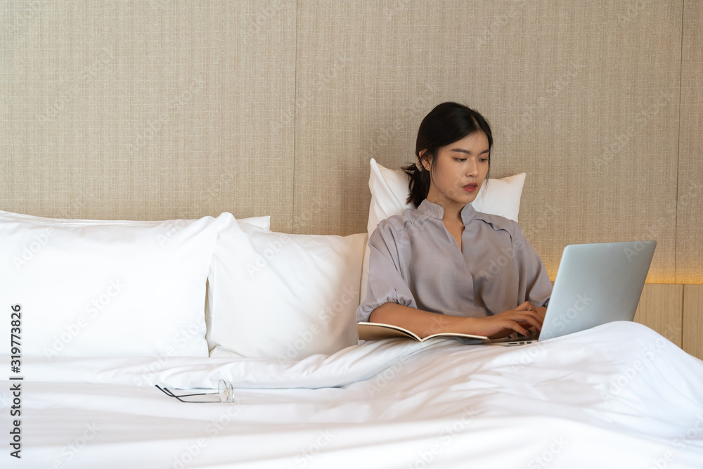 Young asian woman relaxing in the hotel and working with laptop on a bed, Business trip, Working travel concept Young asian woman relaxing in the hotel and working with laptop on a bed, Business trip, Working travel concept