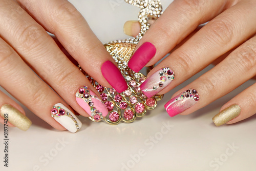 A luxurious manicure with a pink matte finish for nails and a gradient from white with gold to pink nail Polish.Nail art with various shaped rhinestones and colors.