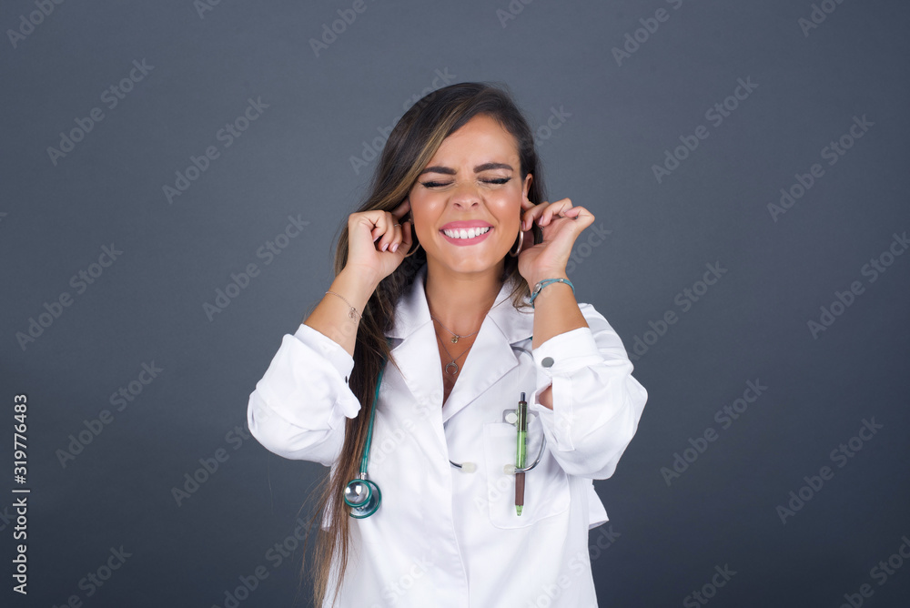 Stop making this annoying sound! Headshot of stressed out young doctor woman, plugging ears with fingers, irritated with loud noise coming from neighbors who live above her. Stop making this annoying sound! Headshot of stressed out young doctor woman, plugging ears with fingers, irritated with loud noise coming from neighbors who live above her.