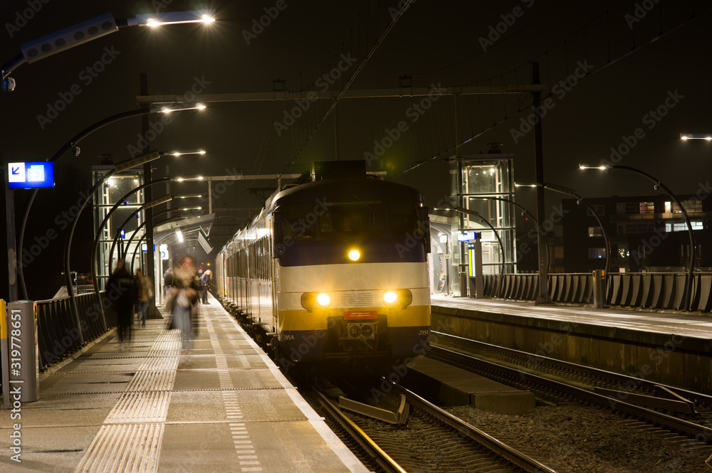Obraz premium Train is waiting on platform and passengers are getting on and off at night, Netherlands