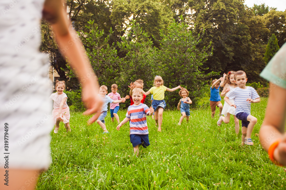 Fototapeta premium Group of children of boys and girls run in park on green grass