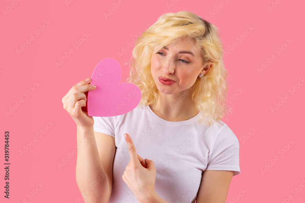 Studio portrait of a young woman pointing at pink heart Studio portrait of a young woman pointing at pink heart