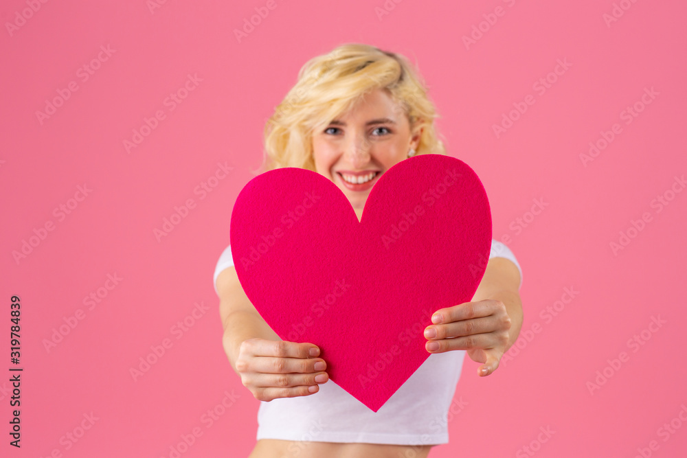 Studio portrait of a smiling young woman holding pink heart, romantic love, dating and Valentine's Day concept Studio portrait of a smiling young woman holding pink heart, romantic love, dating and Valentine's Day concept