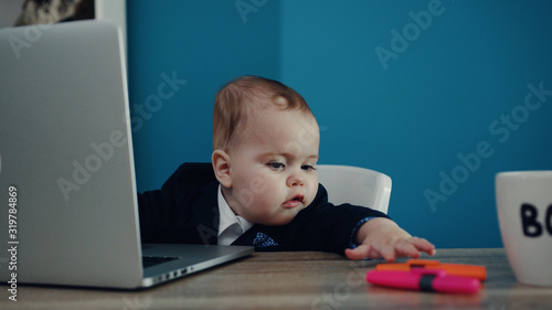 Adorable boss baby working hard by the laptop with notepad and highlighter. Cuteness, toddler boy, successful childhood. Modern office. Joke concept, happiness, playful mood © Fractal Pictures