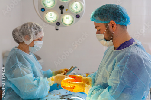 Hospital. Surgeon operates in the operating room. The doctor and nurse disinfect the implant before inserting it during breast augmentation surgery. photo