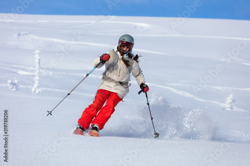Girl On the Ski. a skier in a bright suit and outfit with long pigtails on her head rides outside of the track with swirls of fresh snow. ski freeride, downhill in sunny day. Heliboarding skiing