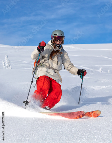 Girl On the Ski. a skier in a bright suit and outfit with long pigtails on her head rides outside of the track with swirls of fresh snow. ski freeride, downhill in sunny day. Heliboarding skiing photo