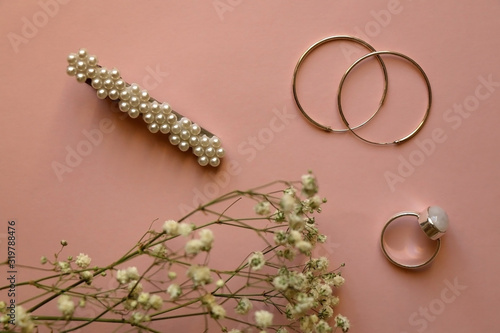 Fashionable accessories on pale pink background. Beret with pearls, silver gemstone ring and hoop earrings, with gypsophila flowers. Top view.