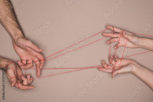 Top view of man and woman holding red string on beige background