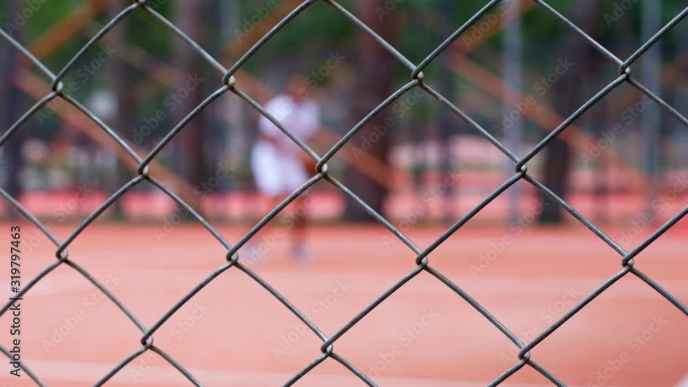 Black young man plays basketball on red outdoor court in the park. Fenced playground. Defocused person Black young man plays basketball on red outdoor court in the park. Fenced playground. Defocused person